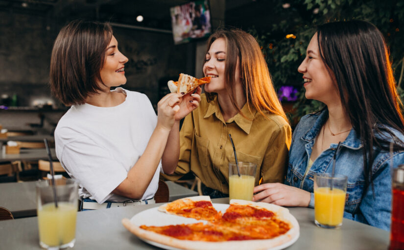 Amigas comiendo pizza en un bar
